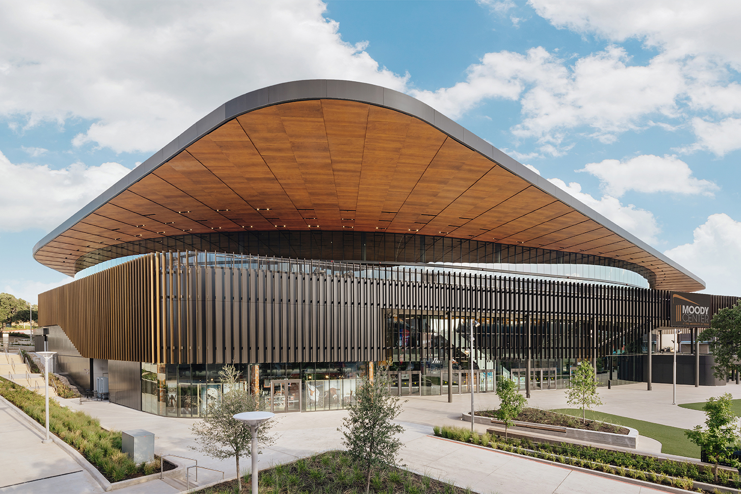 Warm wood tones and crisp MCM paneling ebb and flow in the interior and exterior of Moody Center