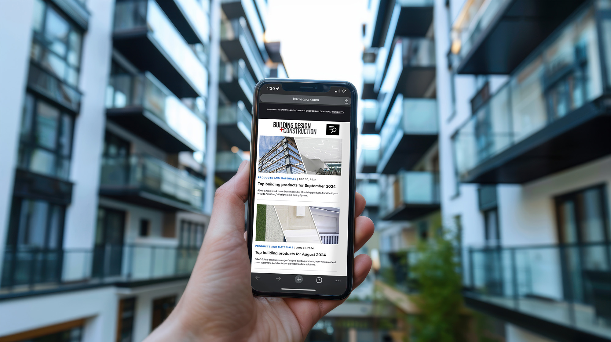 Hand holding smartphone in front of modern apartment building