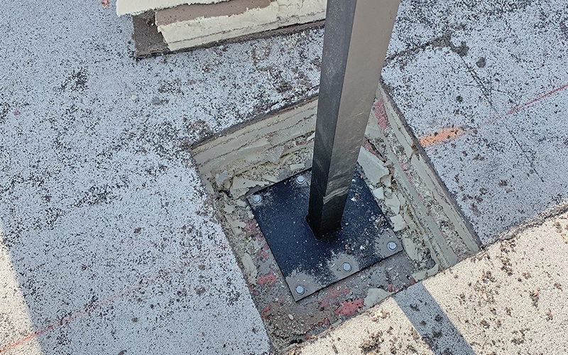 Hole in roof exposes specialized flange plate AVCON engineered to mount Ultra Aluminum commercial railing posts to rooftop terrace.