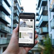 Hand holding smartphone in front of modern apartment building