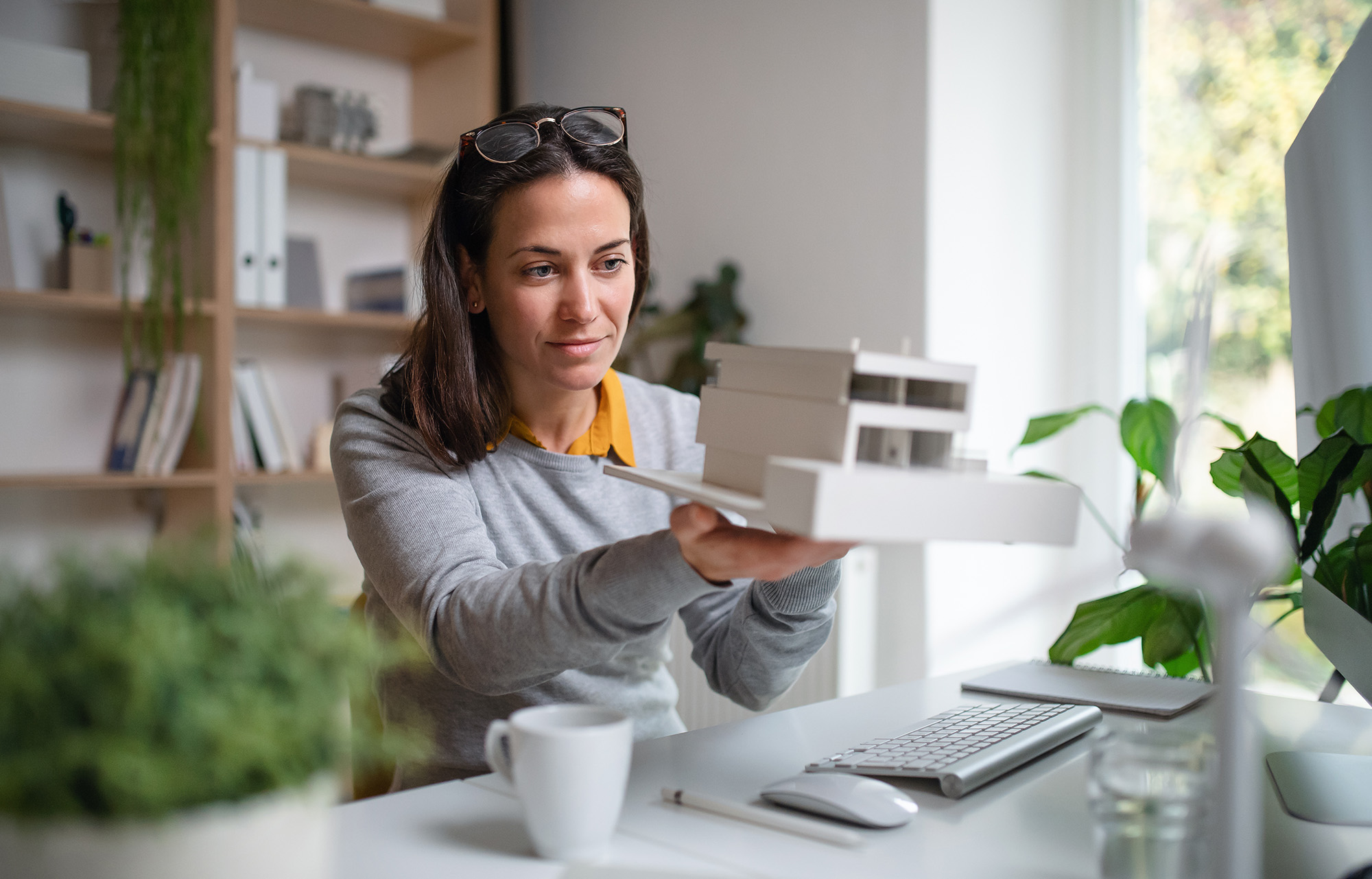 Architect with model of a house sitting at the desk indoors in office